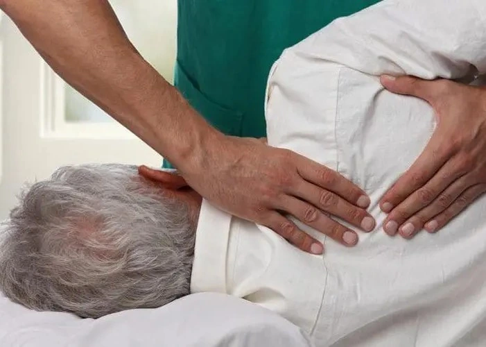 Chiropractor adjusting upper back of elderly patient.