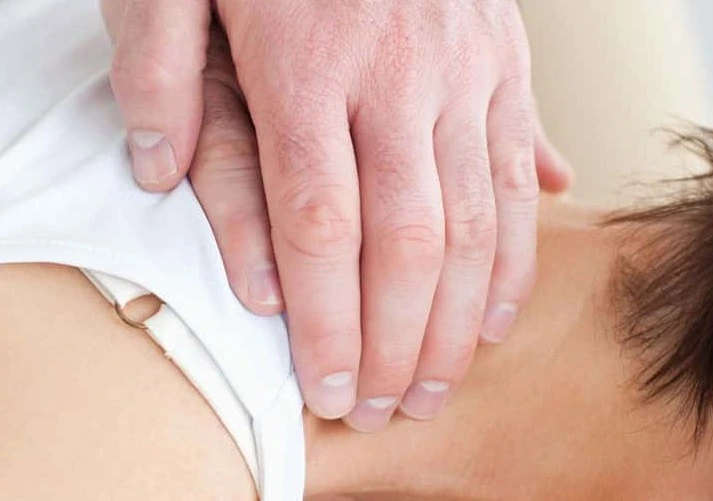 A person in a white sleeveless shirt receives a neck massage to relieve a stiff neck.