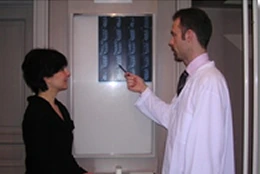 A chiropractor points to an X-ray of a spine while discussing with a patient
